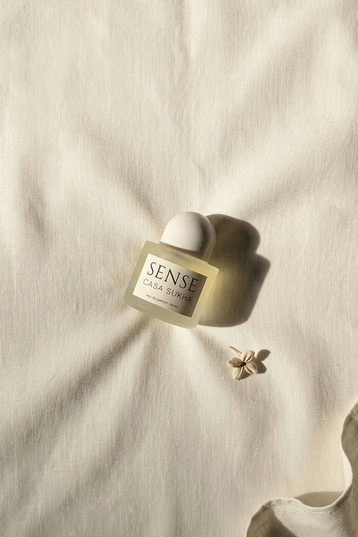 The Sense by Casa Sukha perfume bottle placed alongside soft linen, capturing the warm, sun-drenched atmosphere of a boutique hotel.